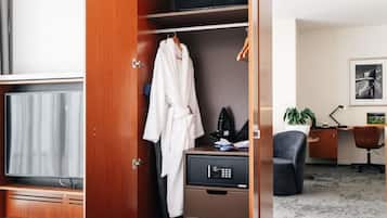 A hotel room with a wooden wardrobe, a TV, a desk with a computer, a chair, and a plant.