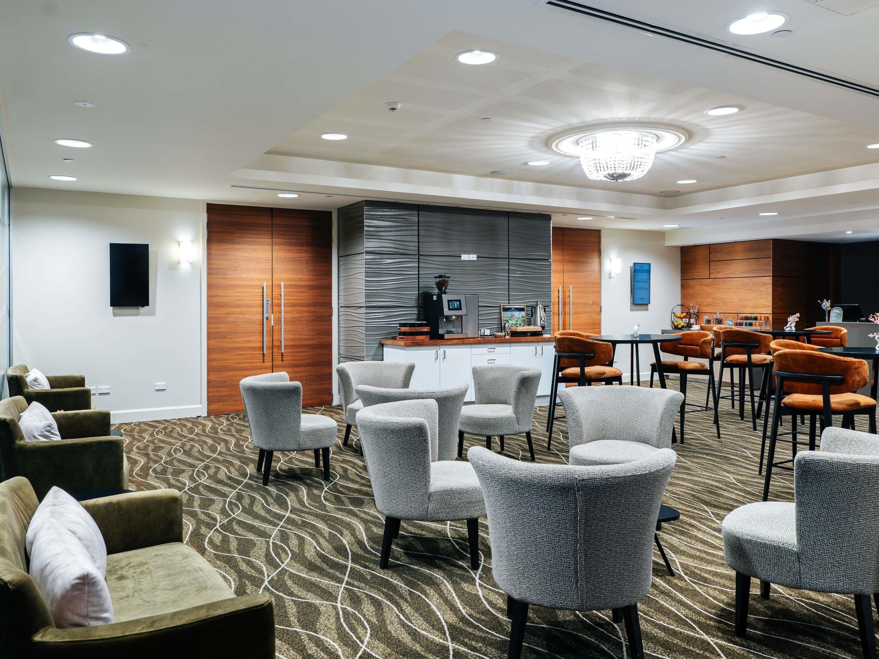 Un hall d’hôtel avec des espaces aménagés pour s’asseoir, un comptoir de réception et, au fond, une cuisine moderne.