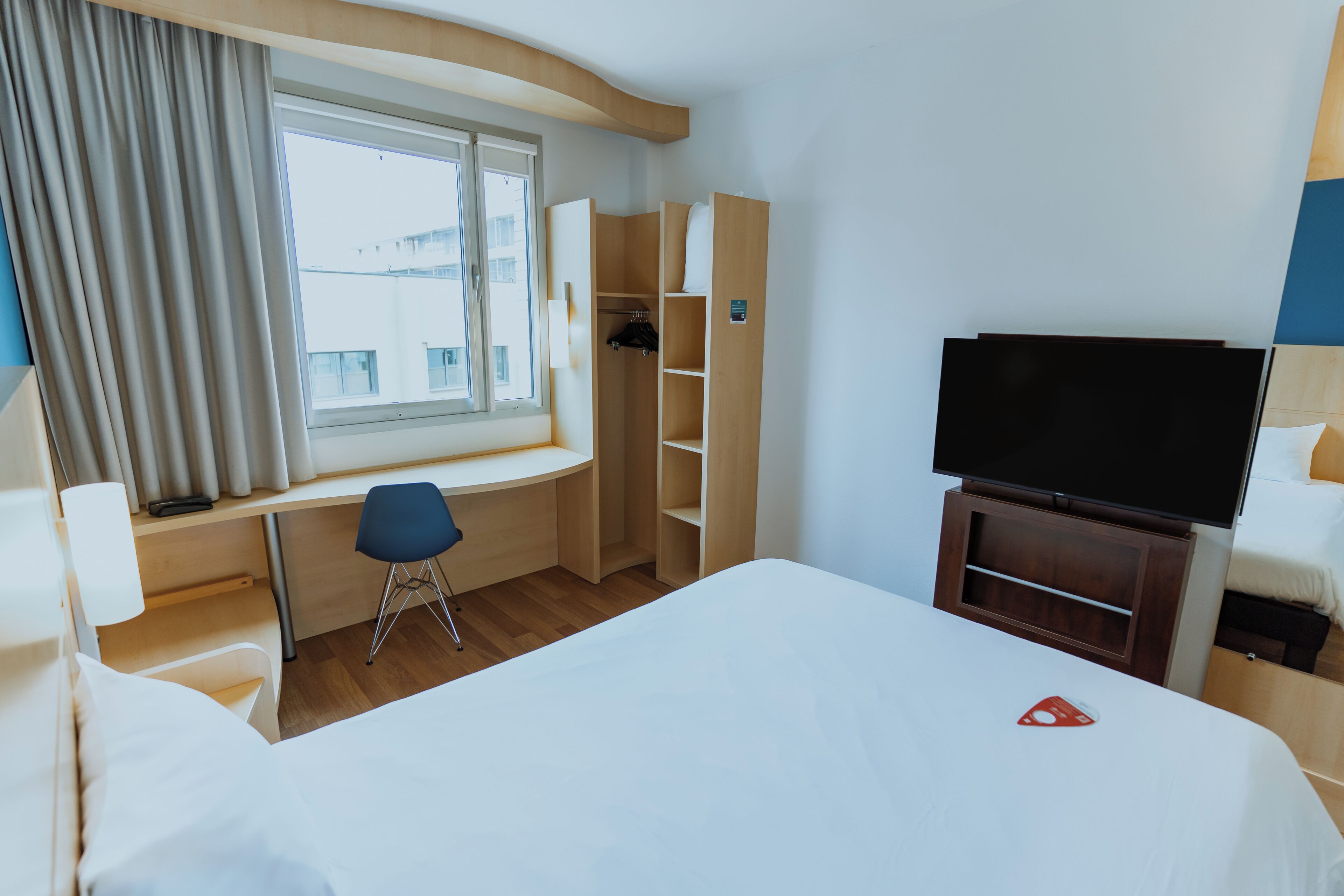 Une chambre d’hôtel avec un grand lit, un bureau avec une chaise, une télévision et une armoire.
