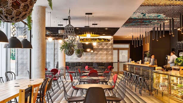 Ein modernes Restaurant mit Schachbrettmuster-Boden, roten und schwarzen Stühlen, hängenden Pflanzen und einer Bar.