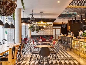 A modern restaurant interior with a checkered floor, red and black chairs, hanging plants, and a bar area. - ibis Barcelona Glories 22 (Barcelona)