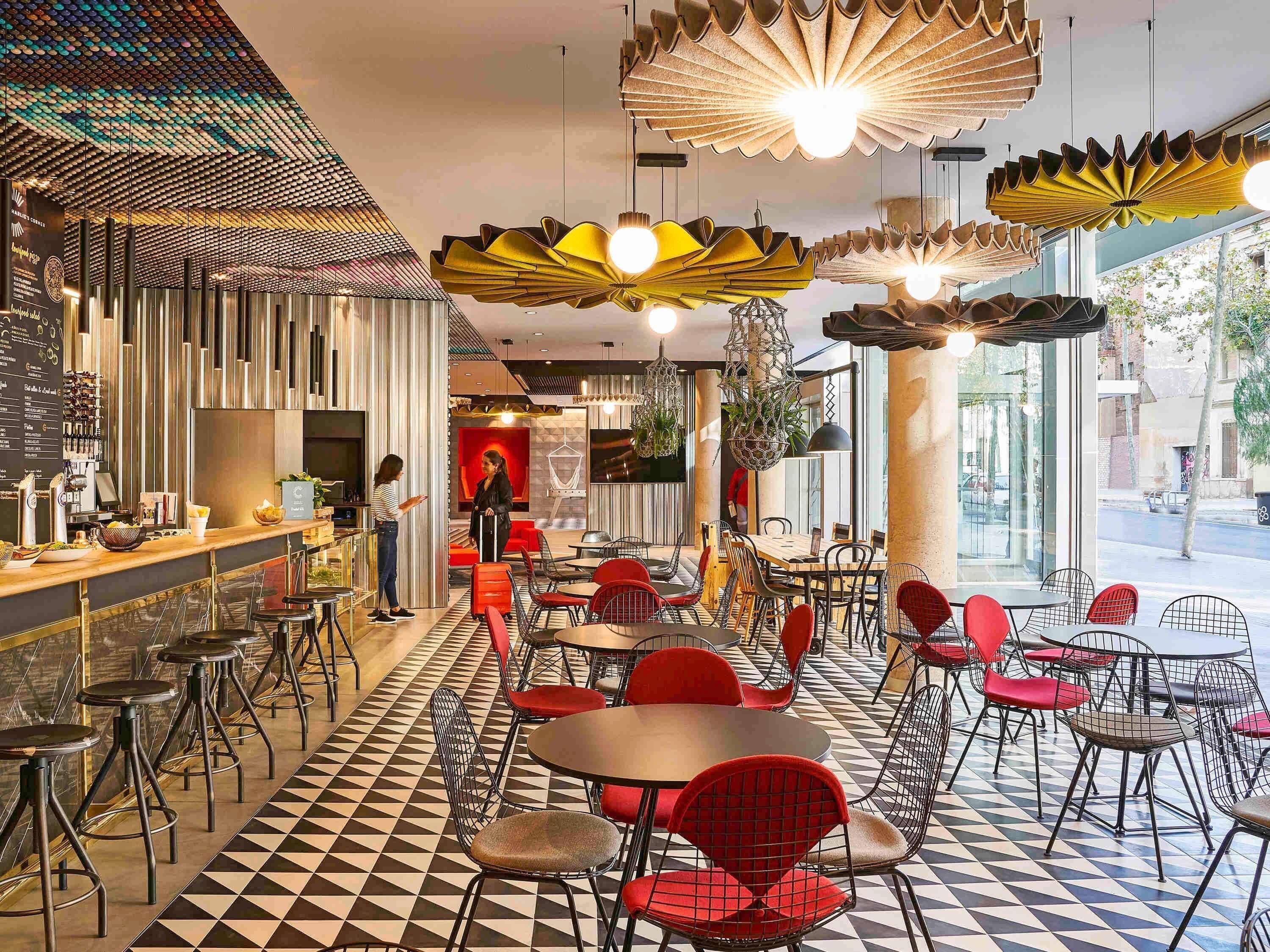 A modern cafe with a checkered floor, red and black chairs, and unique hanging light fixtures.