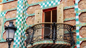 Ein Gebäude mit Schachbrettfliesenmuster, einem Balkon mit aufwendigen Metallgeländern und einem traditionellen Fenster mit Fensterläden.