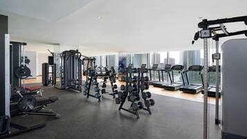 A modern gym with various exercise equipment, large windows, and a city view.