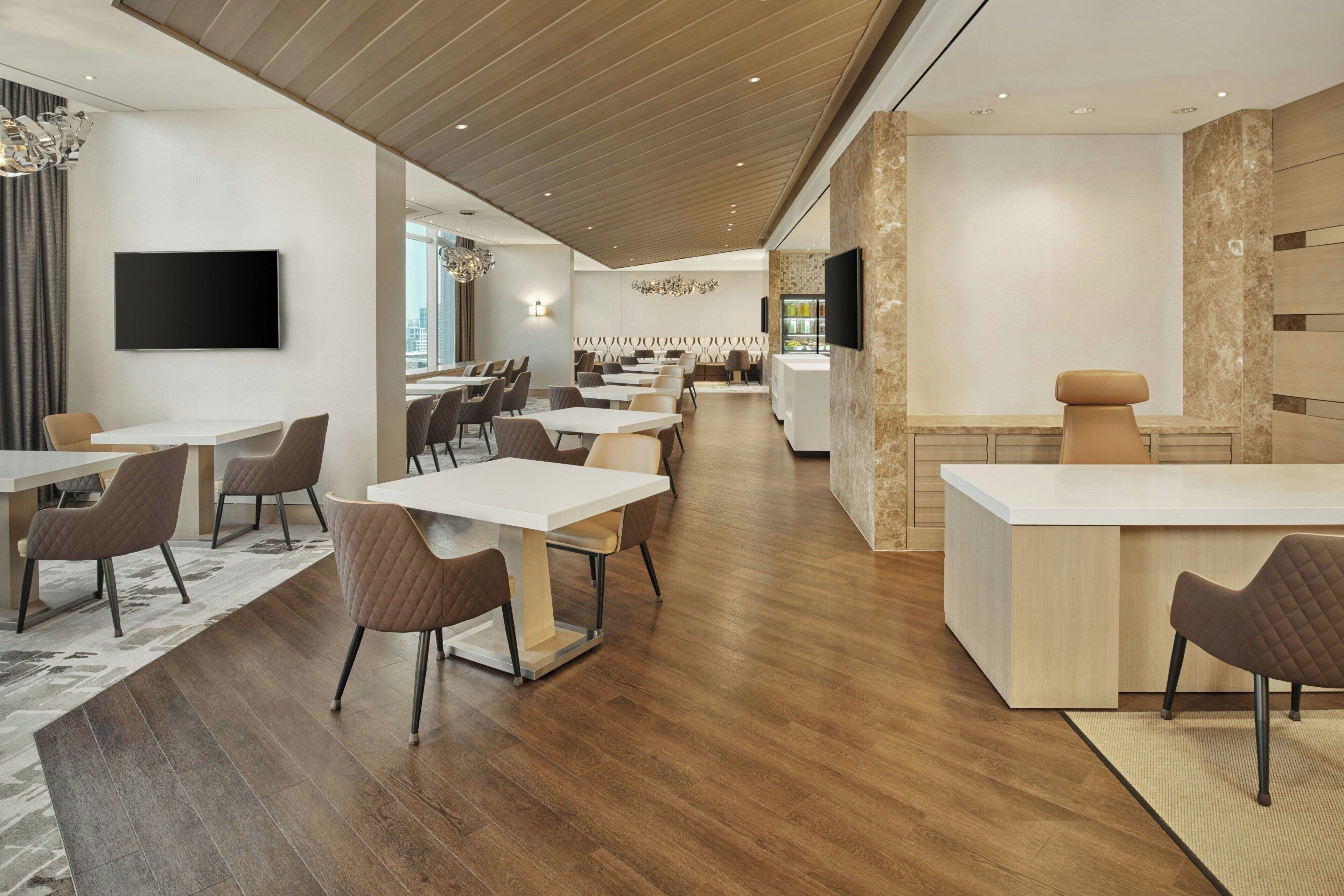 A modern hotel lobby with a reception desk, seating area, and a large TV screen.