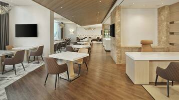 A modern hotel lobby with a reception desk, seating area, and a large TV screen.