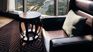 A modern hotel room with a large window offering a city view, a leather sofa, a small round table, and a lamp. - Sheraton Grand Incheon Hotel (Incheon)