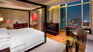 A modern hotel room with a large bed, a desk, and a view of the city at night. - Sheraton Grand Incheon Hotel (Incheon)