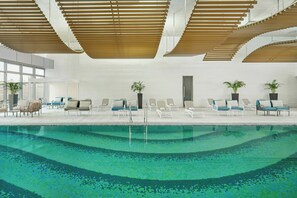 A modern indoor swimming pool with lounge chairs and potted plants.