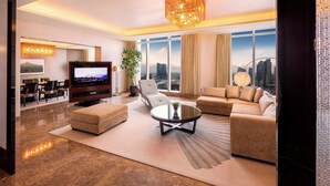 A modern living room with a large flat-screen TV, comfortable seating, a chandelier, and a city view through large windows. - Sheraton Grand Incheon Hotel (Incheon)