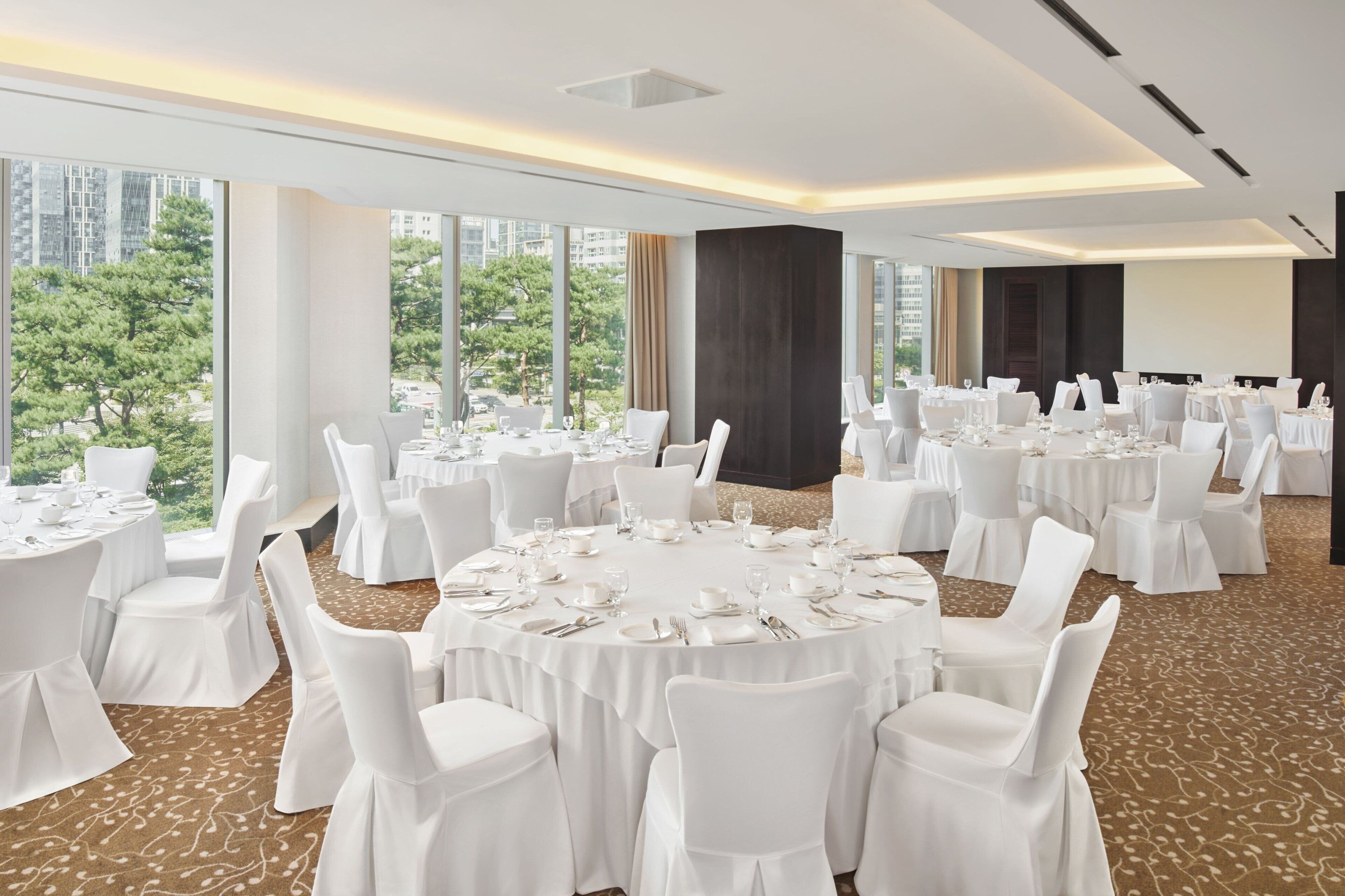 A conference room with round tables, white chairs, and a carpeted floor.