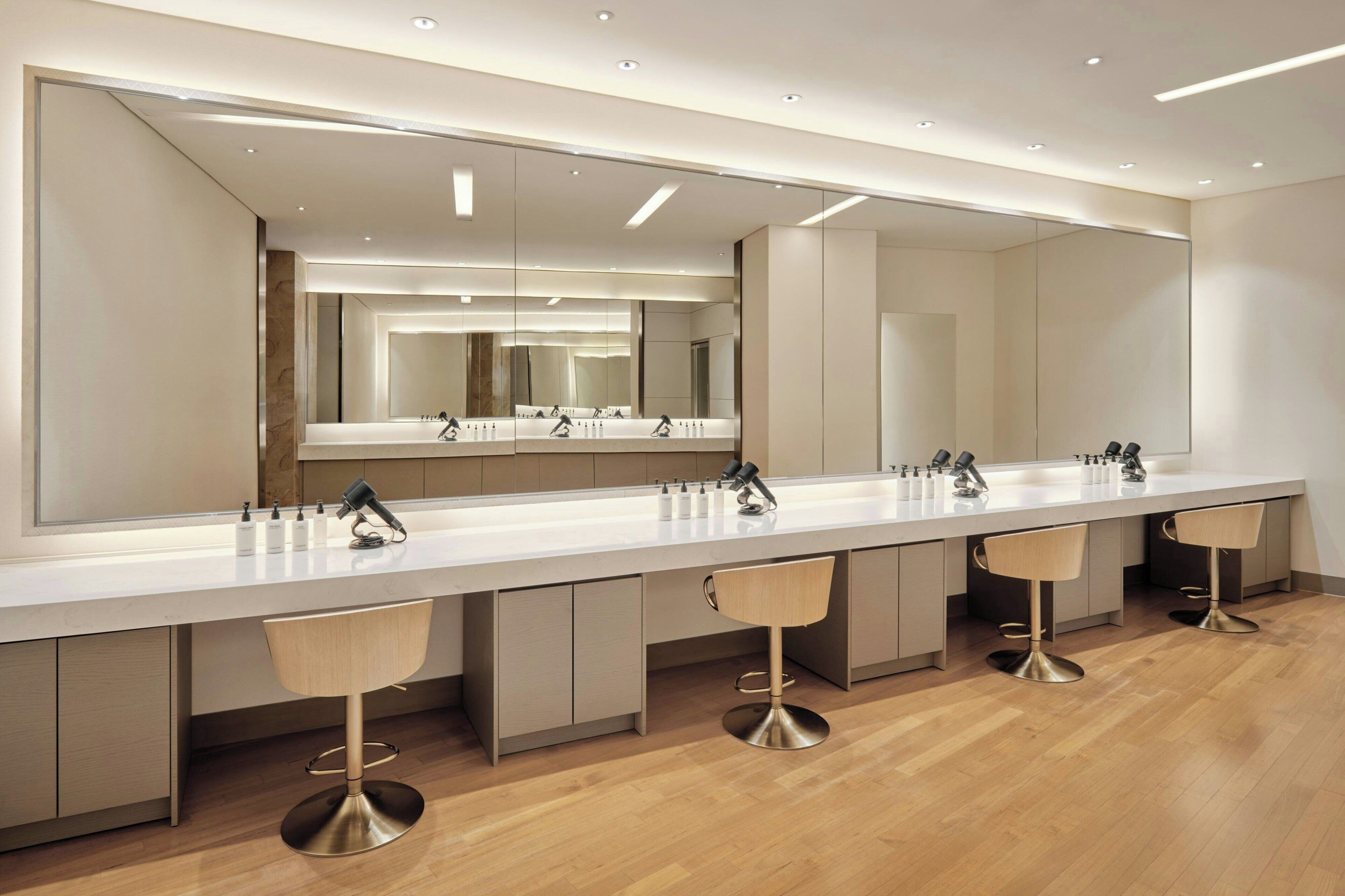 A modern bathroom with a long vanity, multiple sinks, and bar stools.