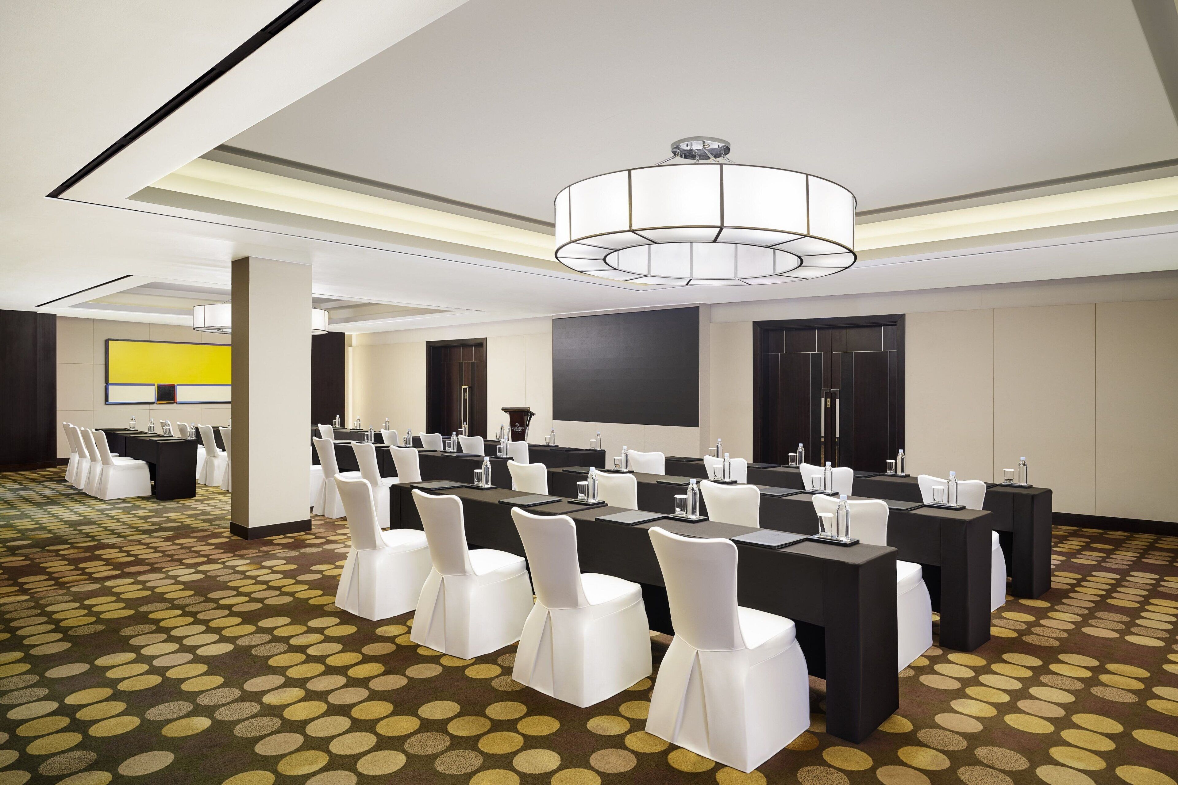 A conference room with multiple tables, white chairs, and a modern chandelier.