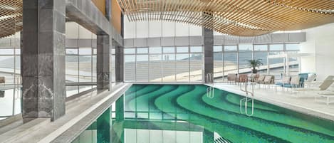 Una piscina de diseño ondulado, rodeada de un interior moderno con amplias ventanas y una estructura de techo de madera.