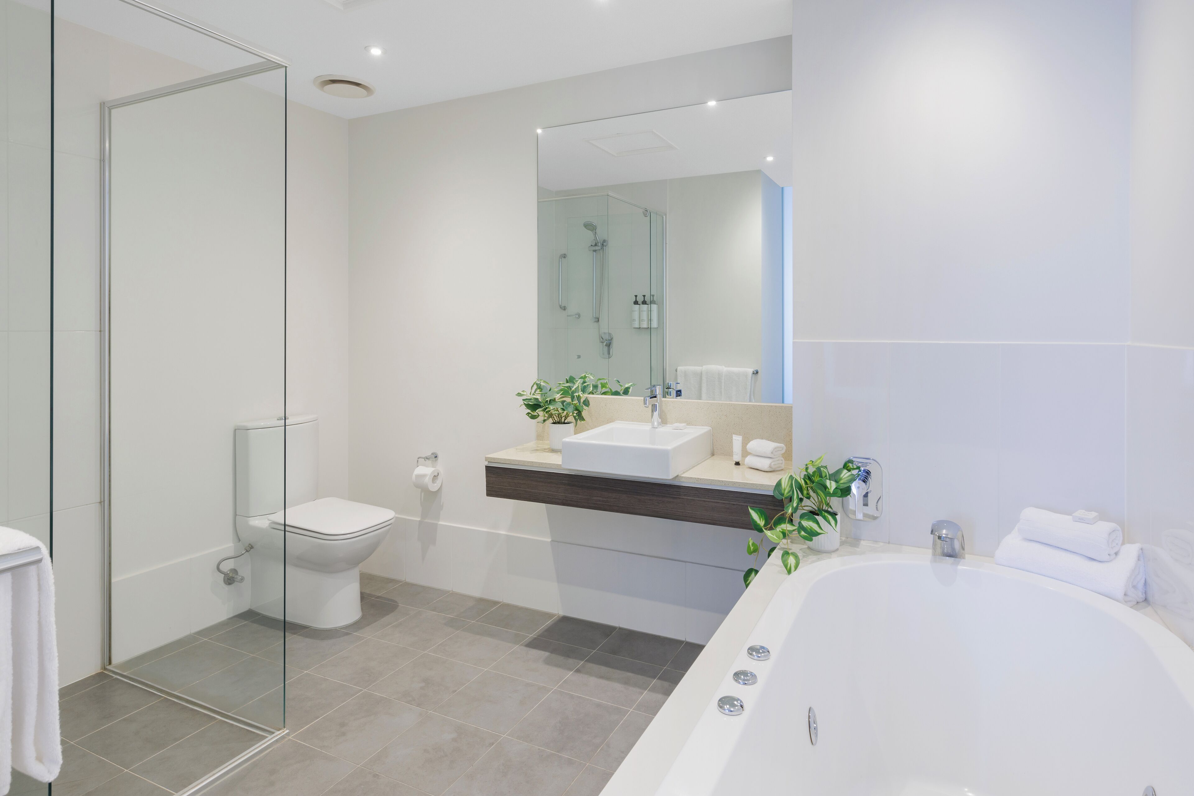 A modern bathroom with a glass-enclosed shower, a white toilet, a freestanding bathtub, and a vanity with a mirror.