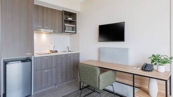 A compact kitchen with a microwave, a refrigerator, and a flat-screen TV mounted on the wall.