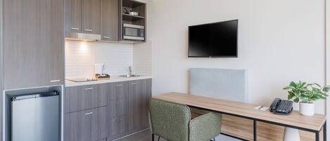 Una cocina compacta con microondas, refrigerador y un televisor de pantalla plana montado en la pared.