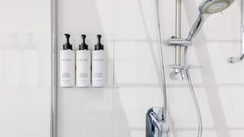 A modern bathroom with a chrome showerhead, a handheld showerhead, and three bottles of MOR body wash and conditioner.