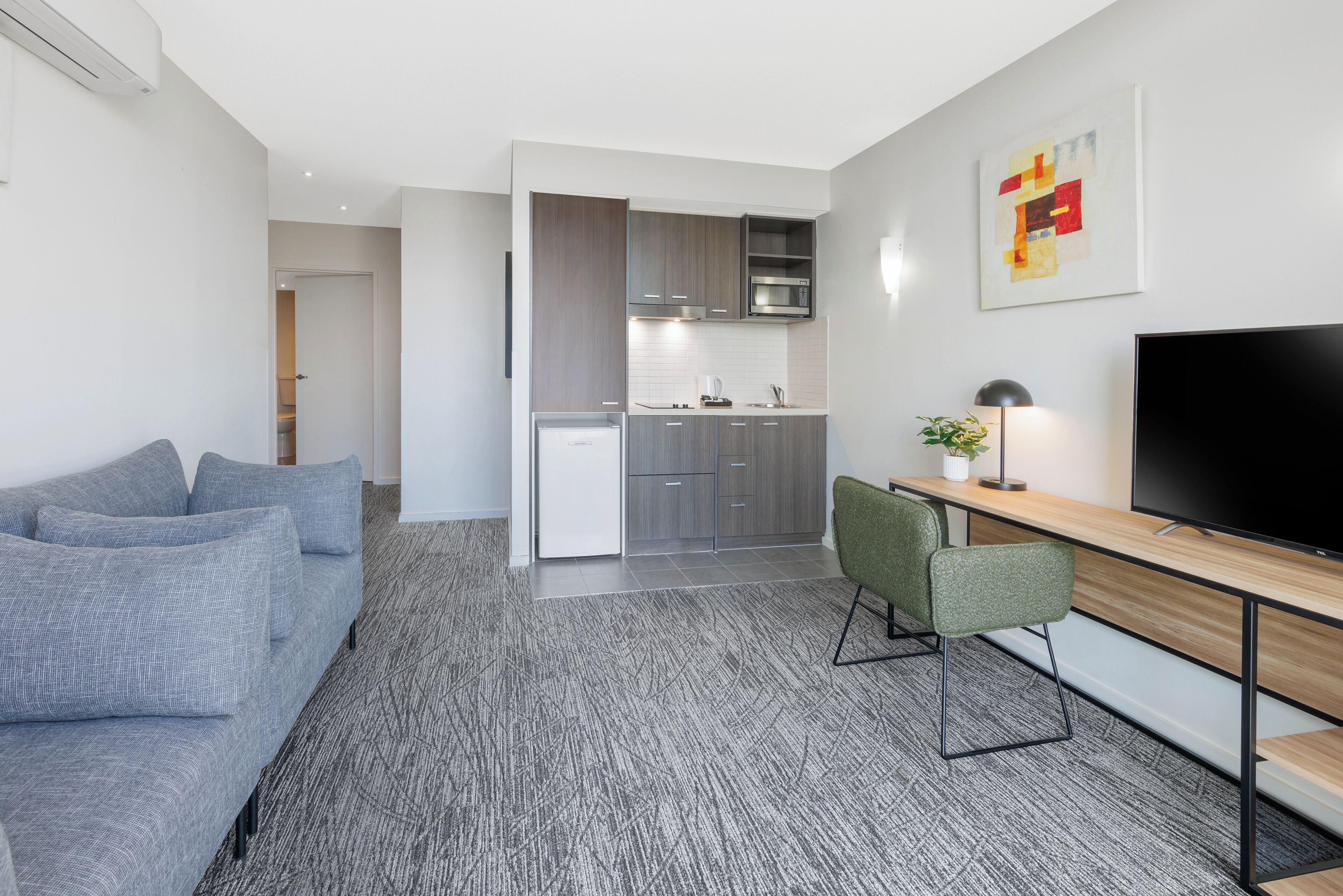 A modern living room with a grey sofa, a wooden dining table, and a TV.