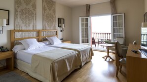 Habitación de hotel con dos camas, un escritorio, una silla y un balcón con vistas.