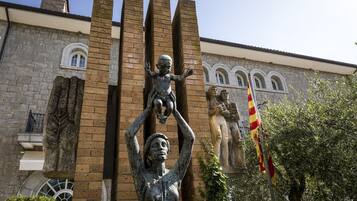 Una estatua de una mujer sosteniendo a un niño frente a un edificio de paredes de piedra y ventanas arqueadas.