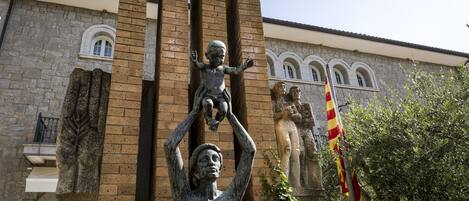 A statue of a woman holding a child in front of a building with stone walls and arched windows.