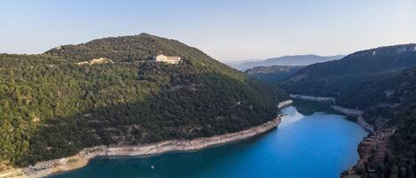Vista aérea de una zona costera con un edificio en una colina que domina una bahía azul tranquila.