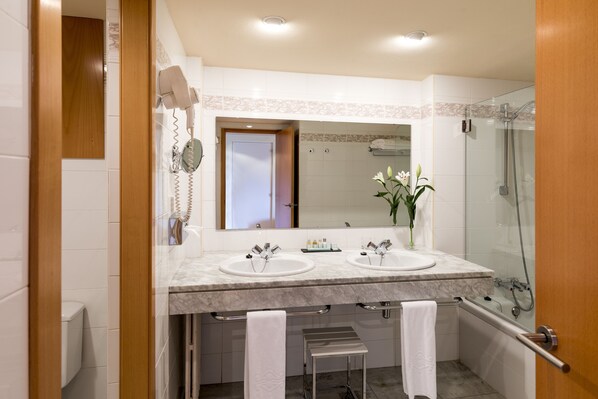 A bathroom with two sinks, a mirror, a shower, and a toilet.