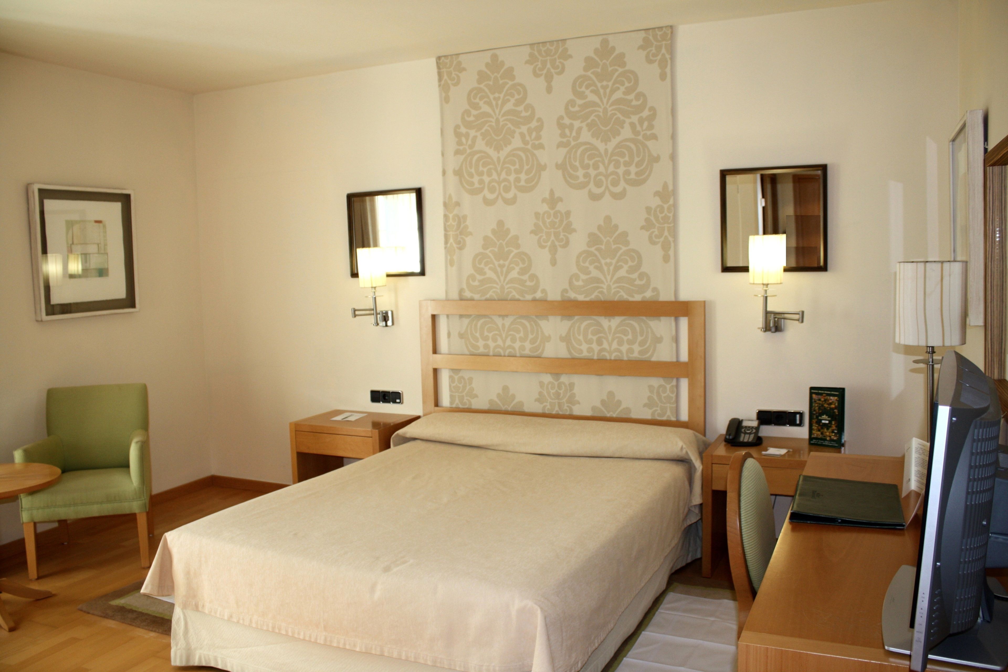 Habitación de hotel con cama, escritorio con computadora, silla, dos mesitas de noche y una lámpara.