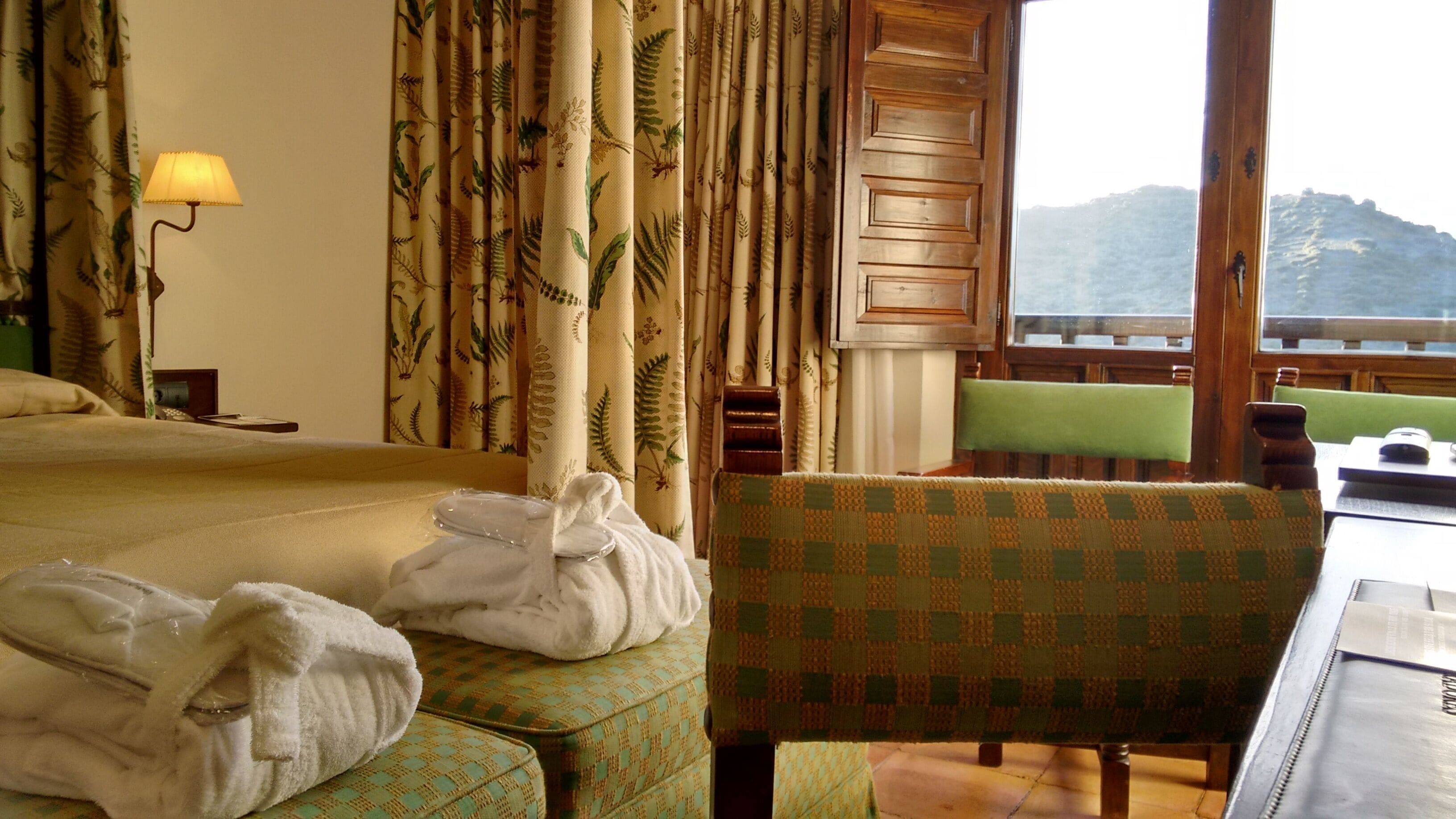 Ein Hotelzimmer mit Bett, Stuhl, Tisch und Blick auf einen Berg.
