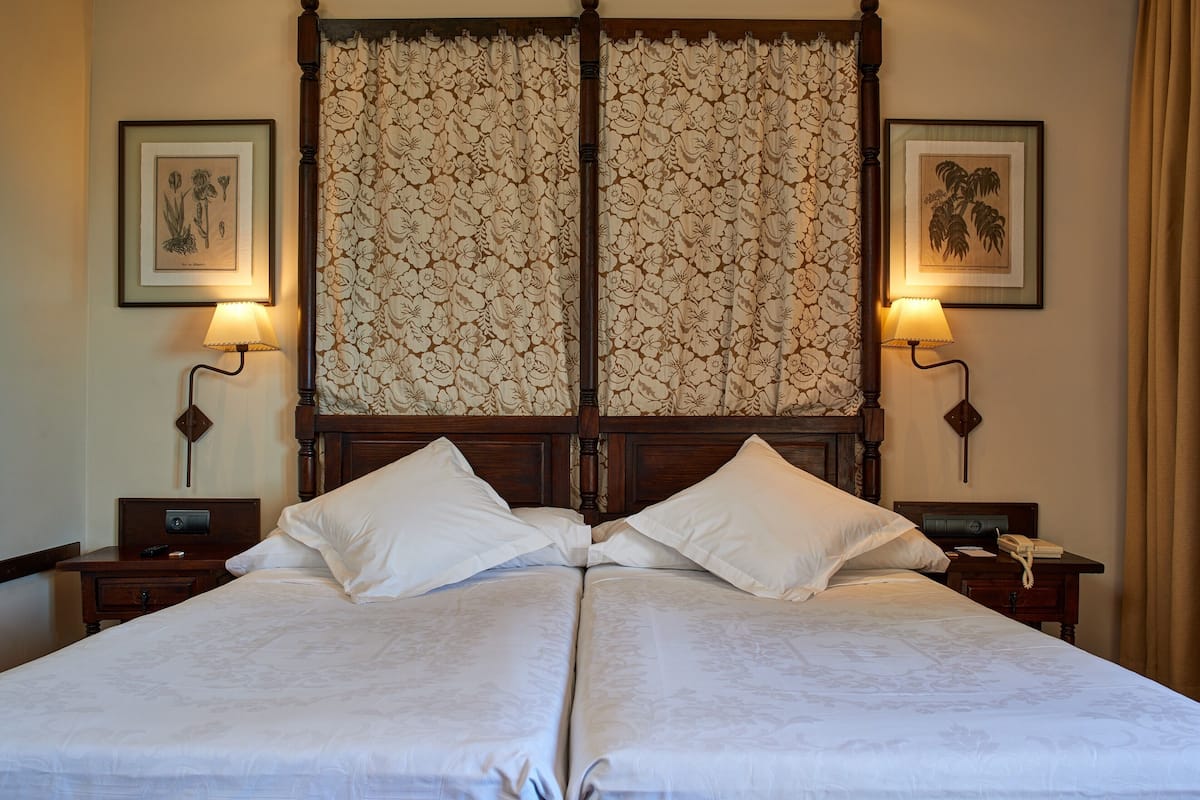 A double bed with a wooden headboard, two bedside tables with lamps, and framed botanical prints on the walls.