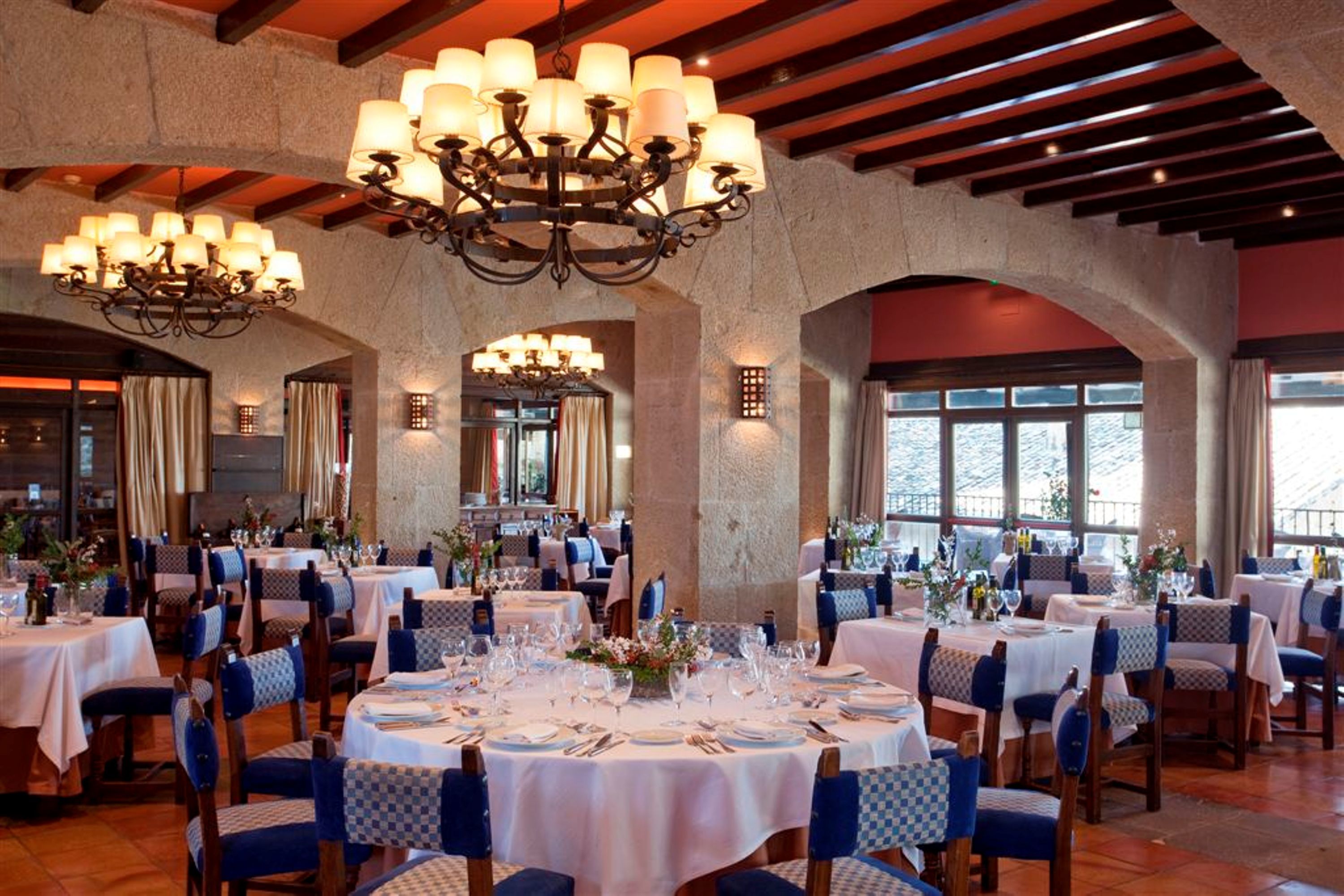 Un restaurante con mesas redondas dispuestas para comer, candelabros y paredes de piedra.