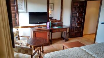 A hotel room with a bed, a desk with a television, a chair, a small table, and a door.