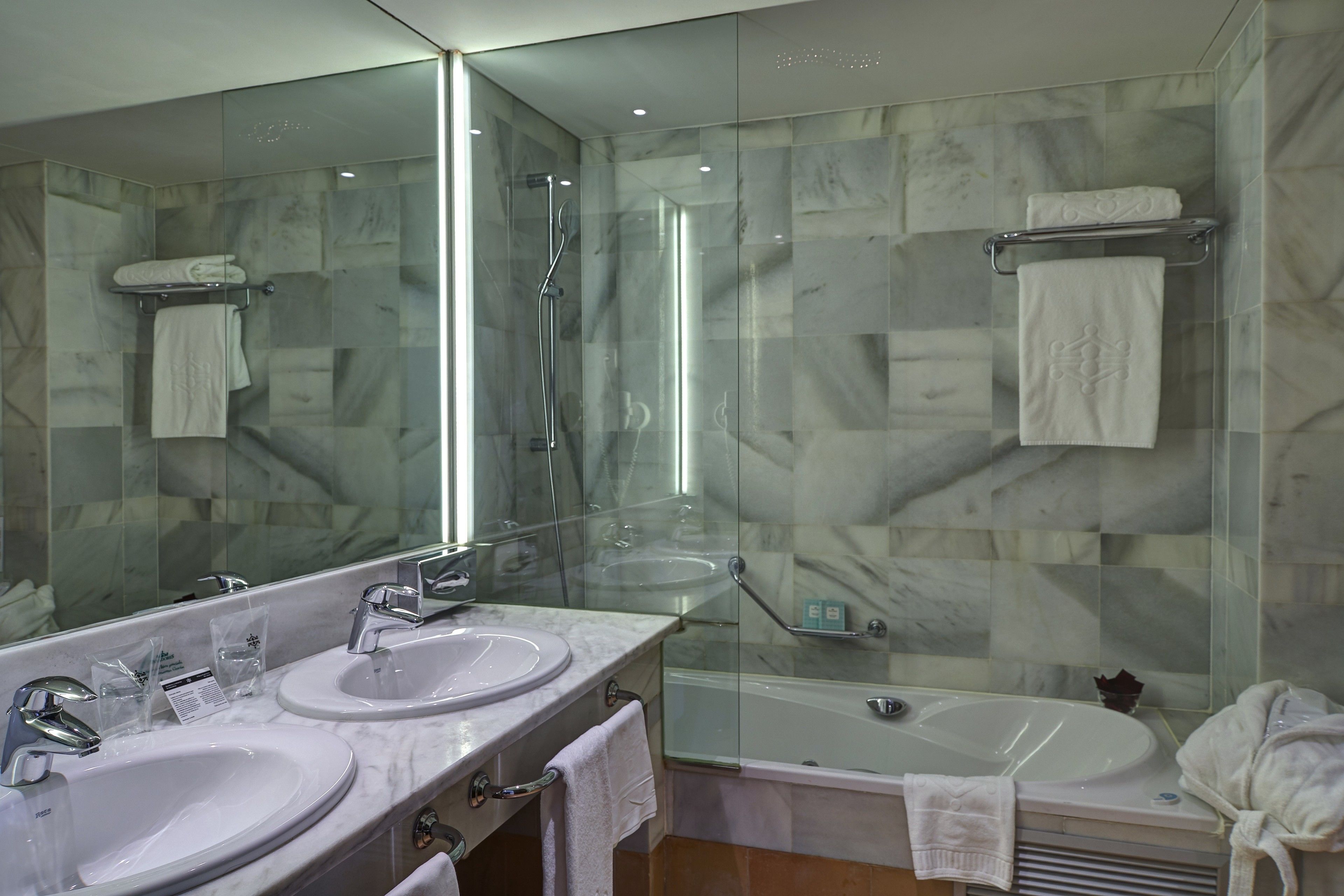 A modern bathroom with two sinks, a glass-enclosed shower, and a bathtub.