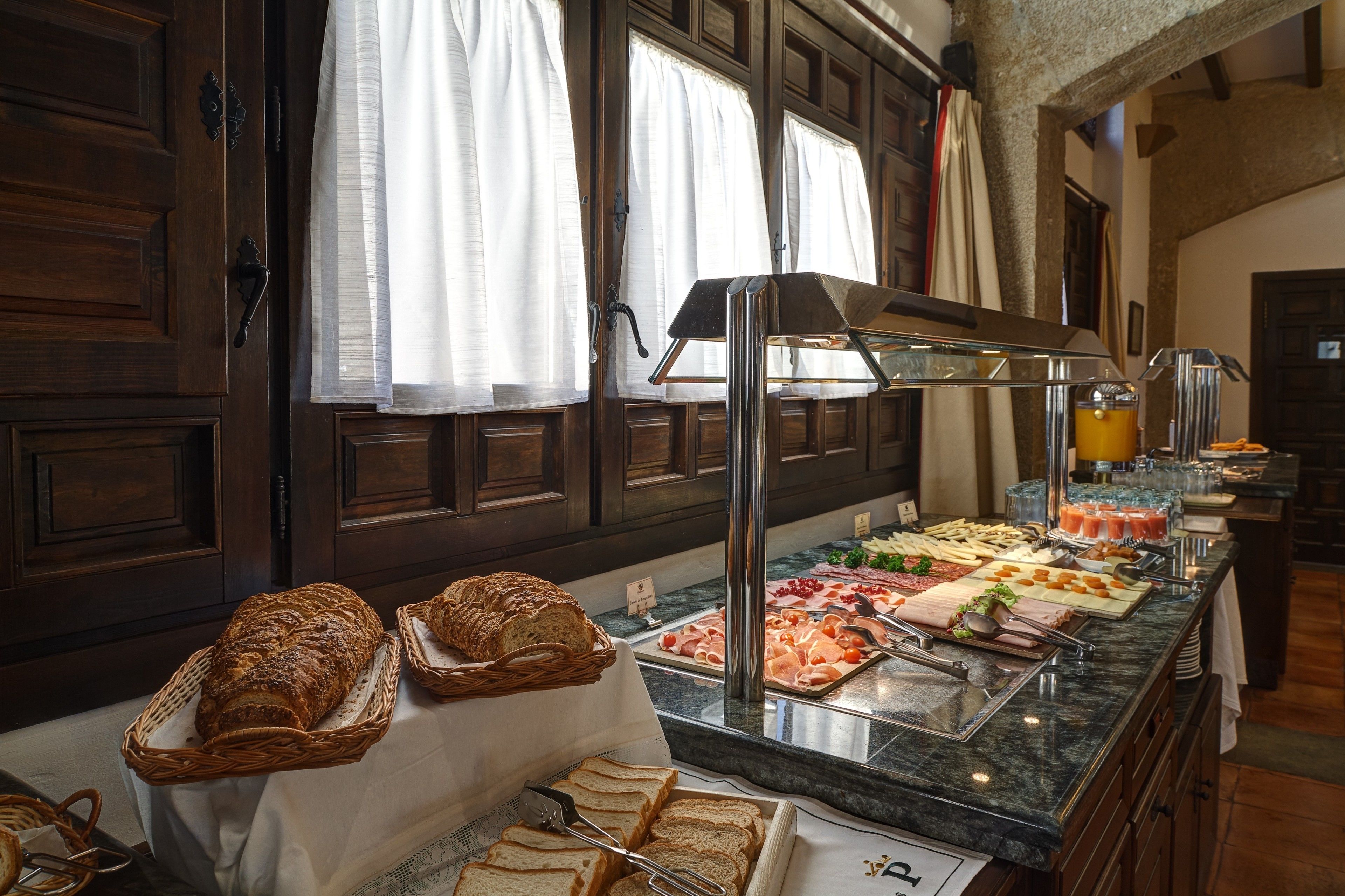 Un buffet proposant une variété d’aliments, notamment du pain, de la viande et des fruits, dans une pièce dotée de portes et de fenêtres en bois.