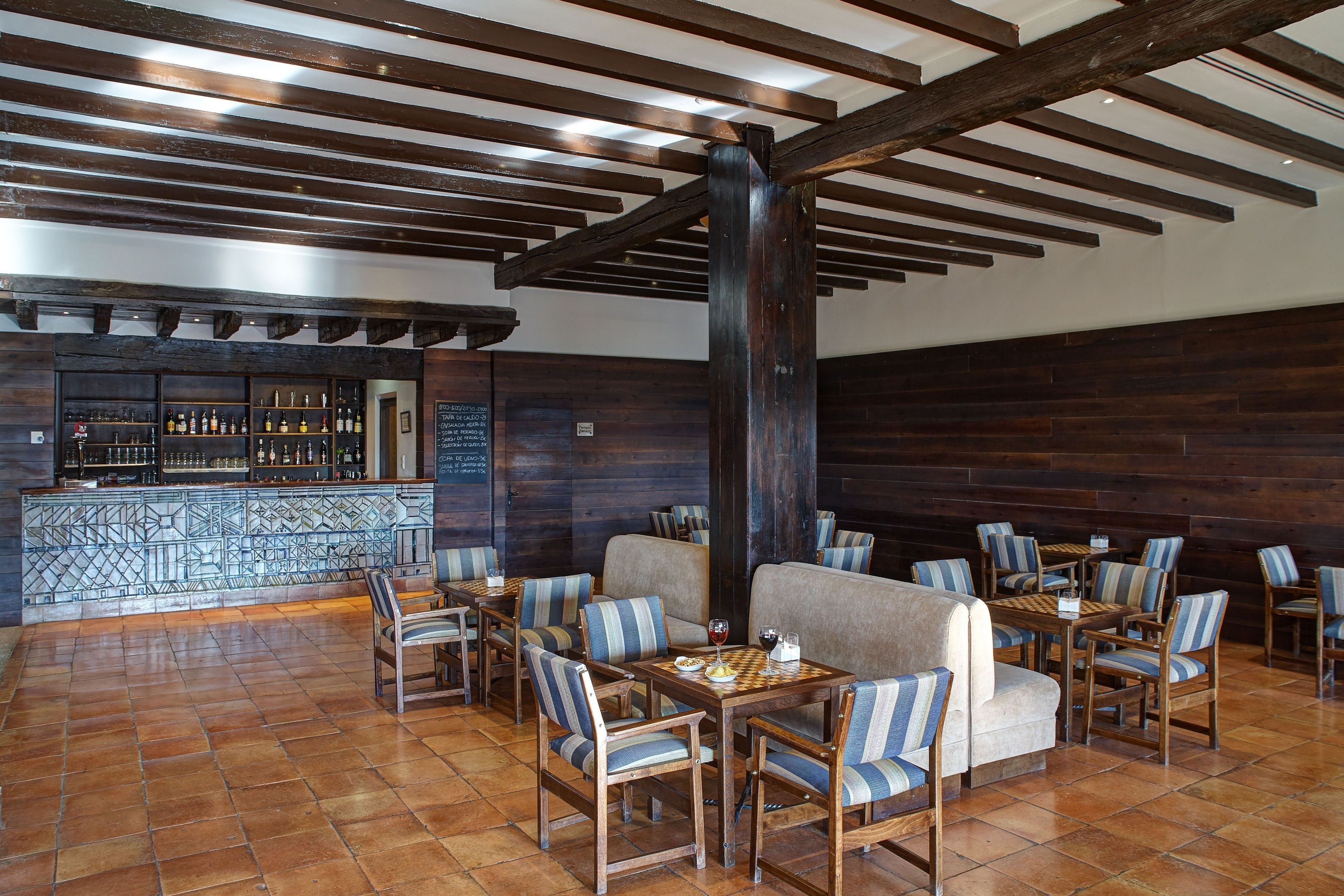 Restaurante com vigas de madeira, piso de azulejos e bancos acolchoados com padrão listrado.