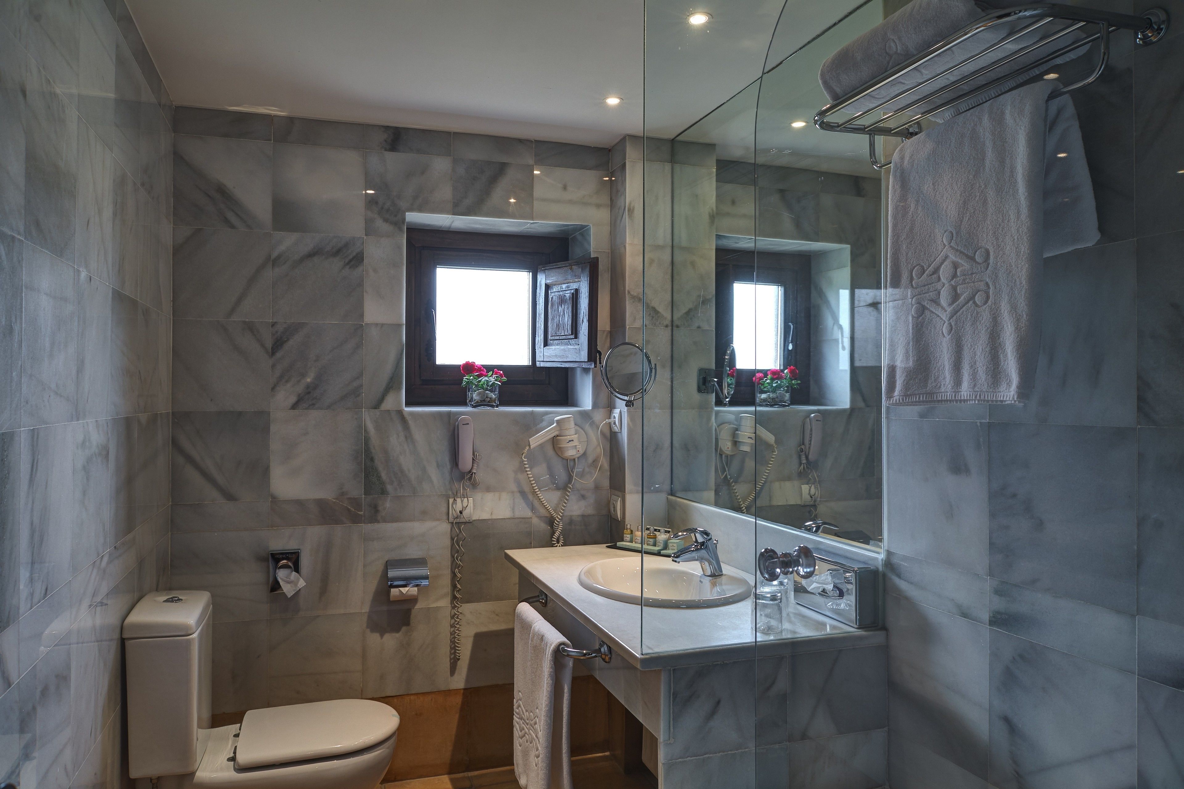 Een moderne badkamer met een marmeren wand, toilet, wastafel met spiegel en een handdoekrek.