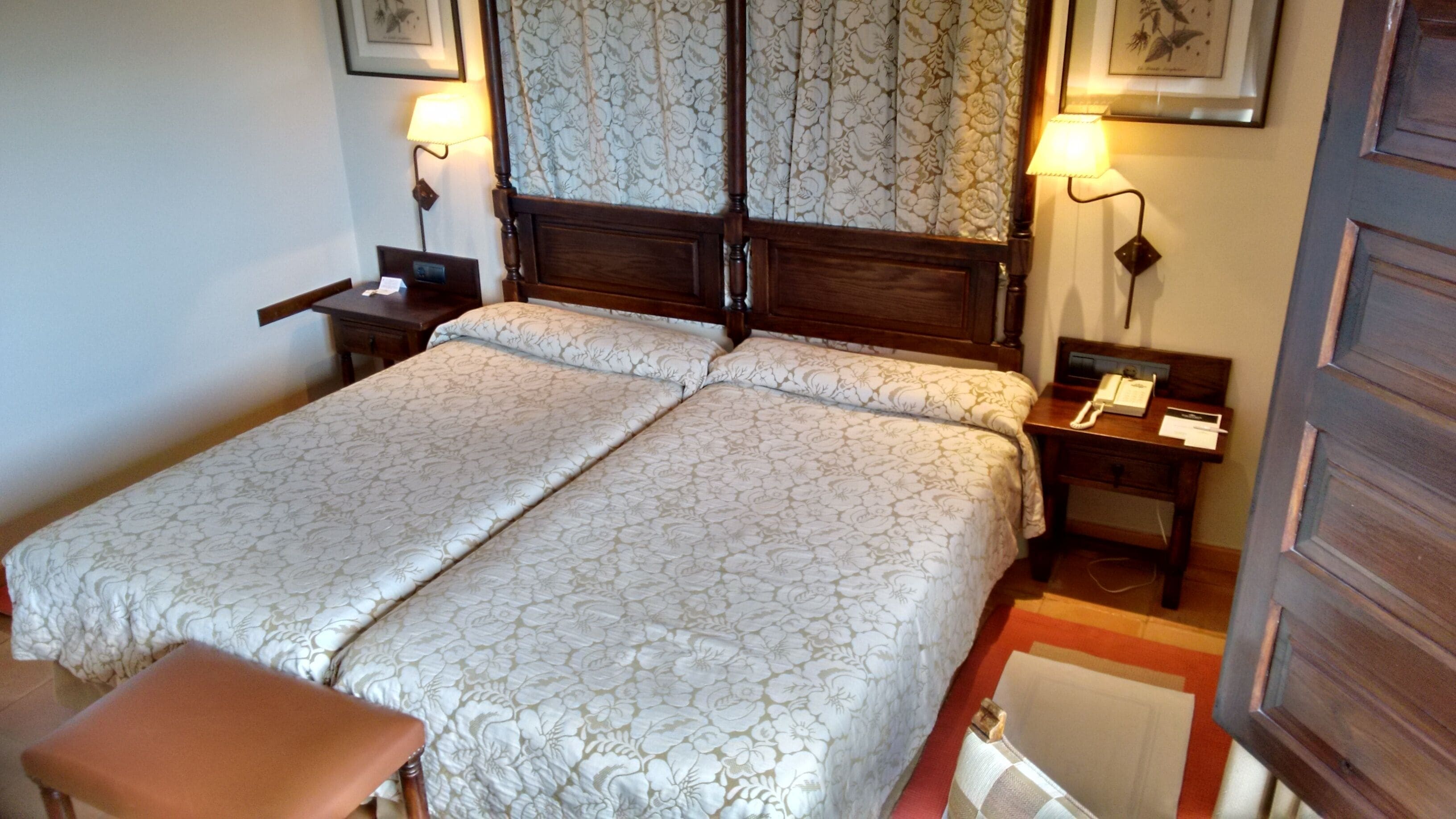 A double bed with floral bedding, a nightstand with a lamp, and a bedside table with a telephone.