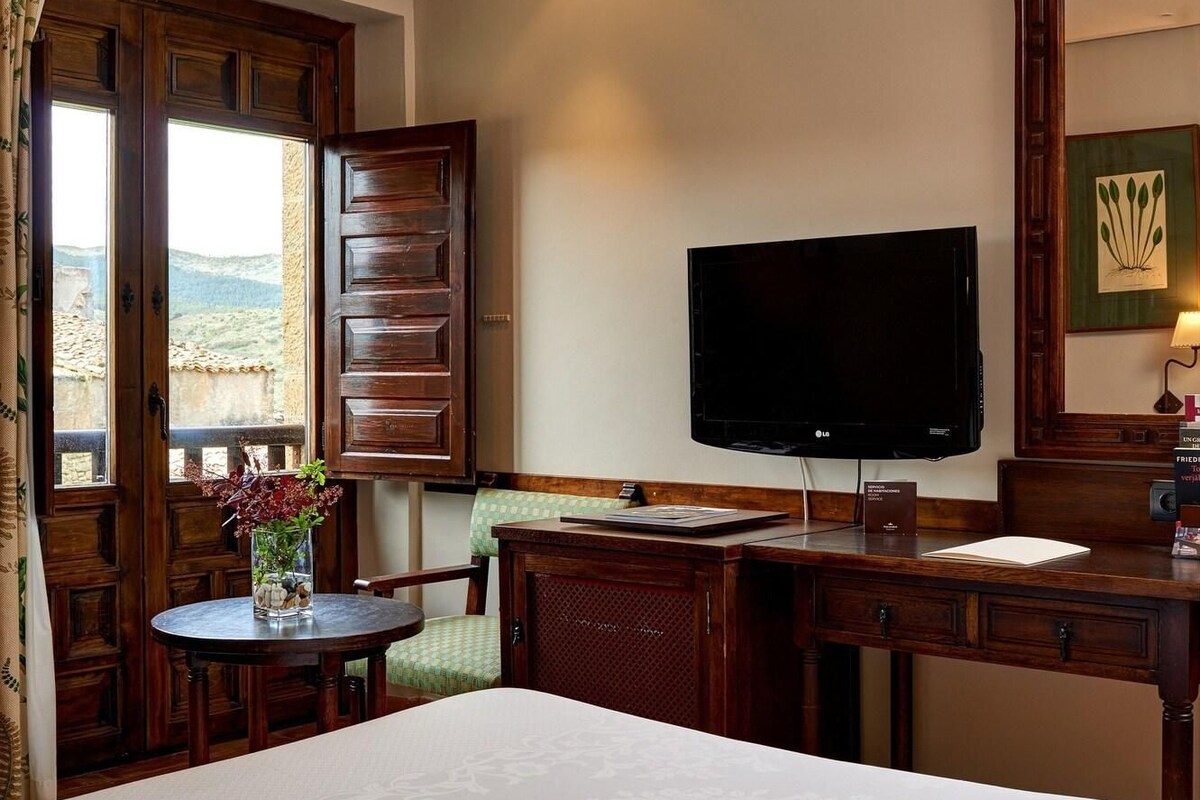 A hotel room with a bed, a desk, a television, and a window with a view.