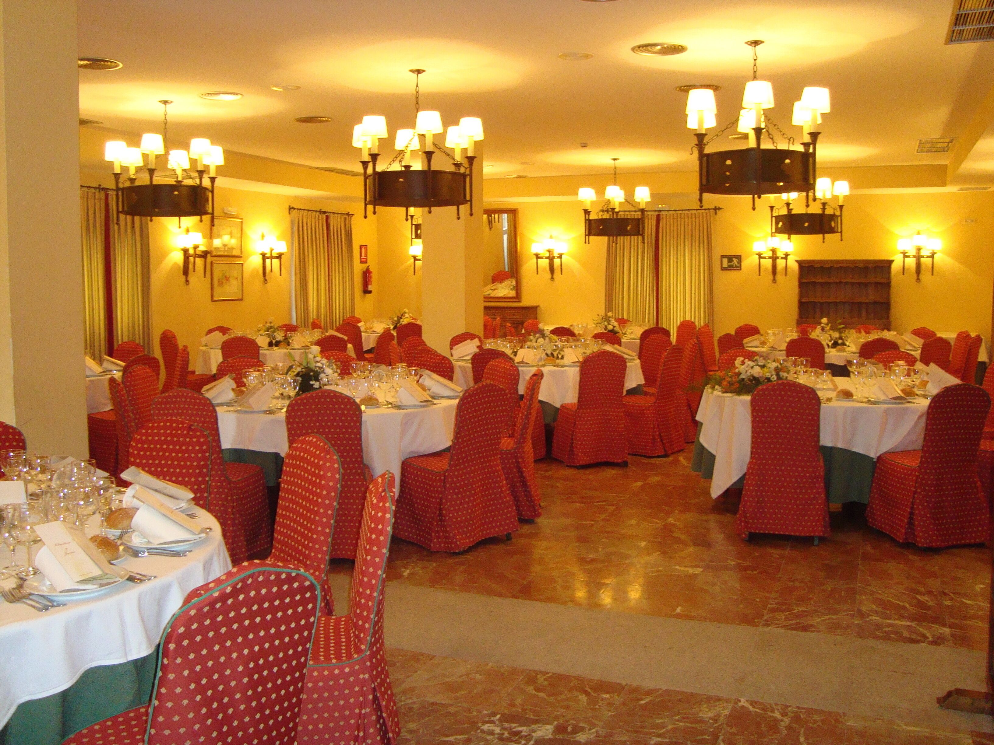 Un comedor formal con varias mesas dispuestas para el servicio, sillas rojas y candelabros.