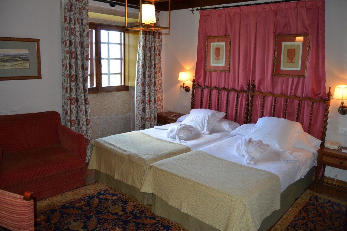 A double bed with a wooden headboard, two bedside tables, a red armchair, and a patterned carpet.