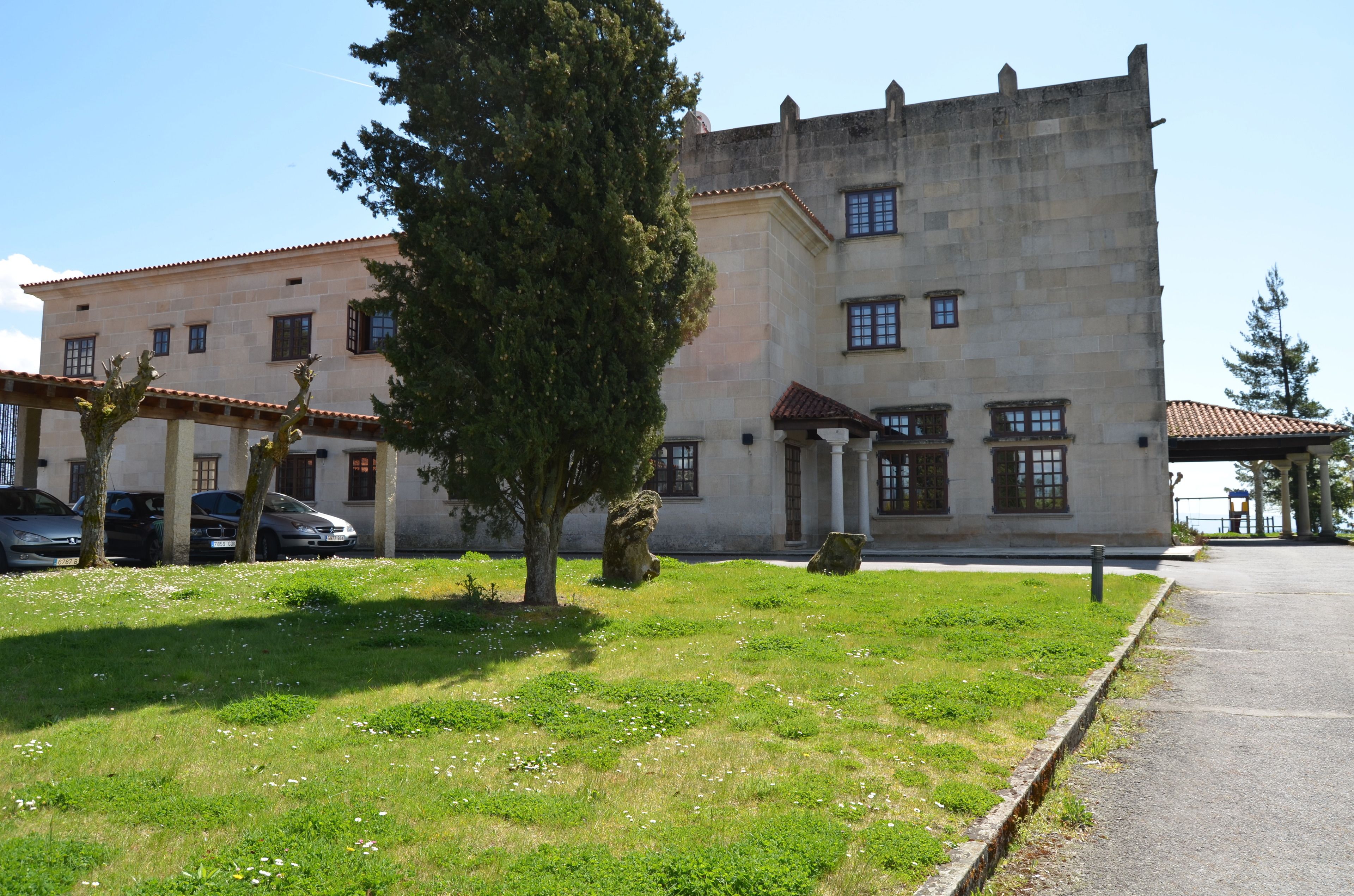 A historic building with a stone facade, a large tree in front, and a paved pathway.