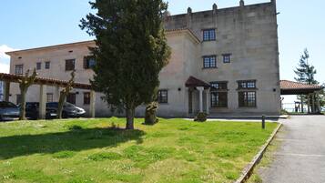 A historic building with a stone facade, a large tree in front, and a paved pathway.