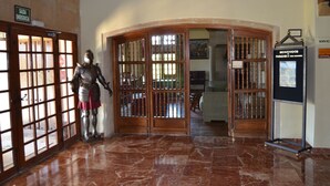 A marble-floored entrance with a knight statue, wooden doors with glass panels, and a welcome sign.