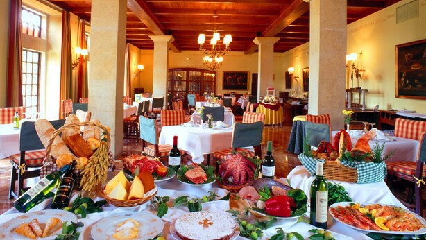 A restaurant with wooden beams and chandeliers, tables set with food and wine.