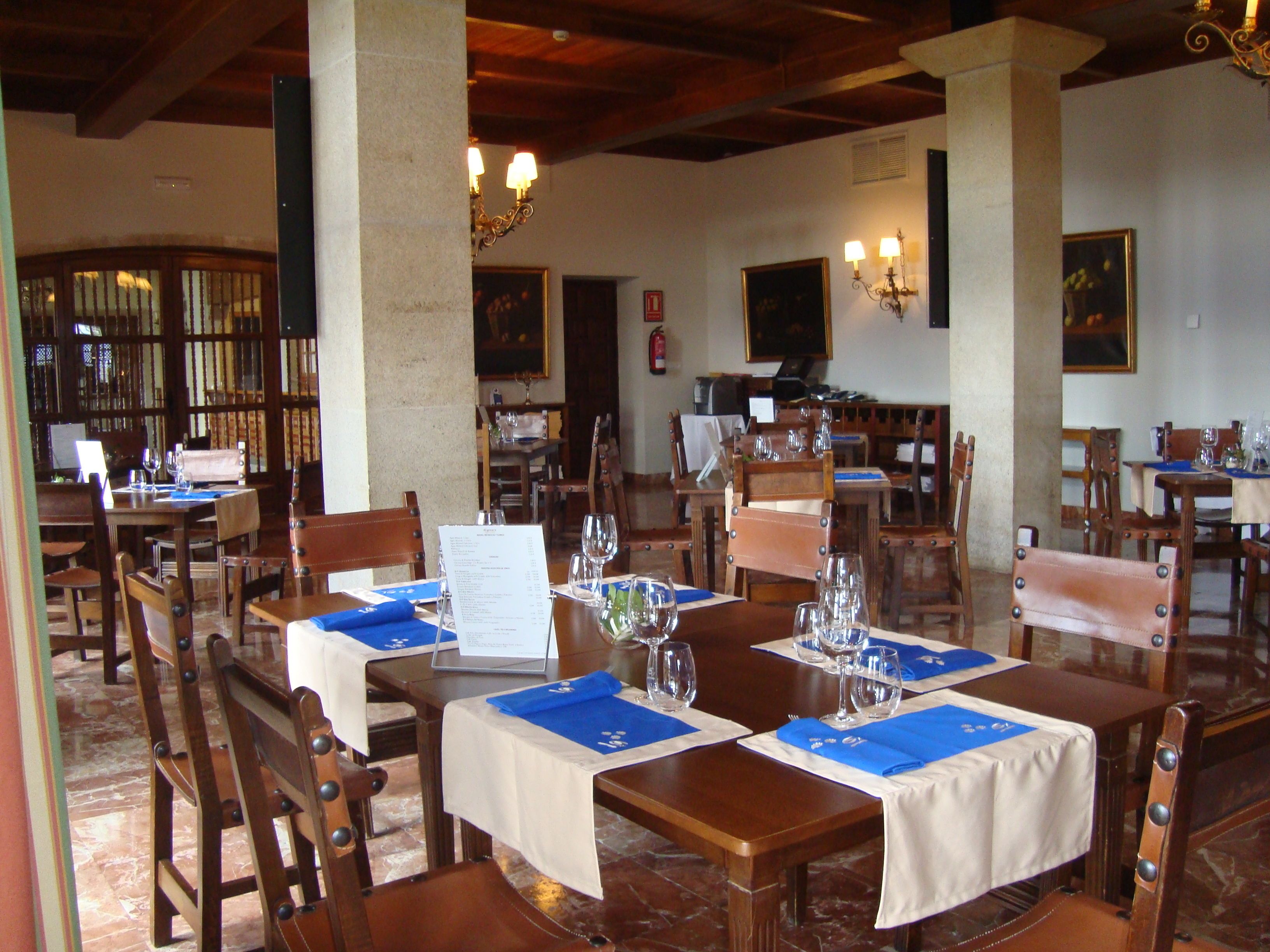 Un restaurante con mesas y sillas de madera, menús y copas de vino listas para recibir comensales.