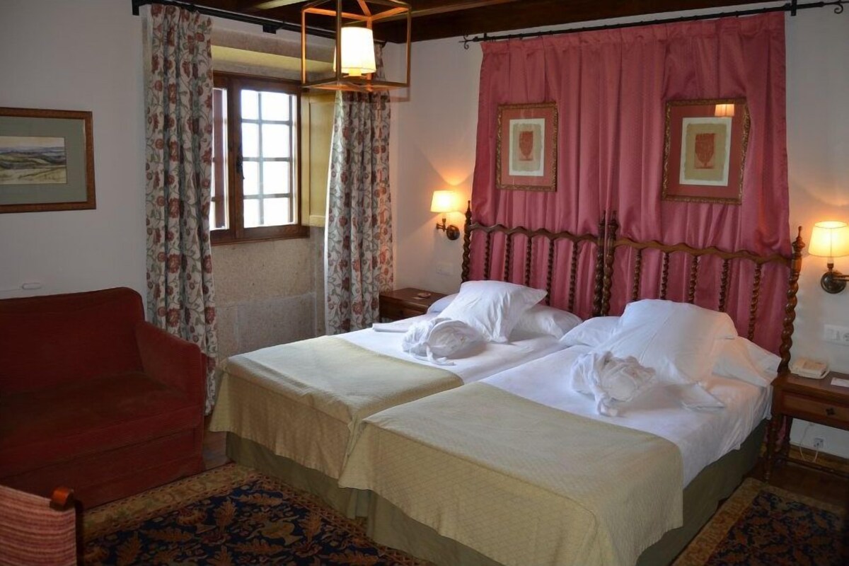 A room with two beds, a red sofa, a patterned rug, and a window with curtains.