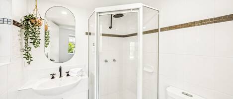 Un bany modern amb dutxa de vidre, un lavabo blanc i un mirall.