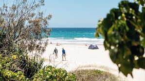 A beach with people, a tent, and vegetation. - Le Beach Apartments (Burleigh Heads)