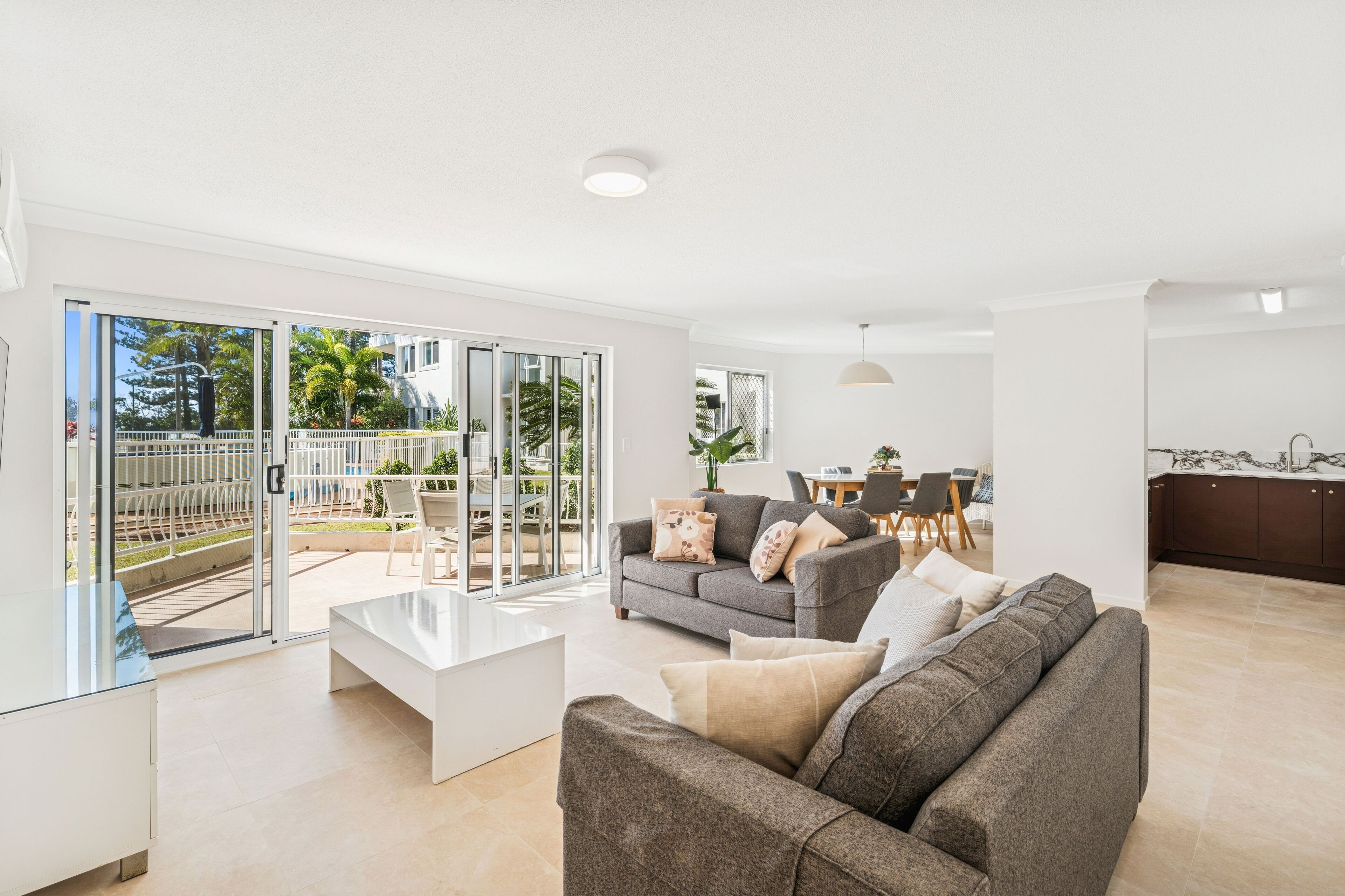A modern living room with a sofa, coffee table, and a dining area with a table and chairs.